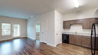 Located at 1000 Cowpen Ct in Williamsburg, VA, this single-floor, 2-bedroom, 2-bathroom residence offers a well-organized layout designed for comfortable living. The kitchen is a standout feature, equipped with dark espresso cabinetry, granite-style countertops, and black appliances including a refrigerator, gas range, dishwasher, and microwave — all set atop rich, dark hardwood-style flooring that flows throughout the main living areas. The open transition between the kitchen and living room creates a cohesive, functional space, with a glass exterior door in the living area providing access to an outdoor area and allowing natural light to pour in. Both bedrooms feature plush wall-to-wall carpeting and large windows that frame views of the surrounding greenery, contributing to a calm and bright atmosphere. The primary bedroom includes a dedicated closet with wire shelving systems for organized storage. The bathrooms are finished with tile flooring and include walk-in showers with grab bars, offering accessibility-conscious design. Two additional closets provide ample storage throughout the residence. The clean white walls and neutral palette create a fresh, move-in-ready environment suitable for a variety of living arrangements.