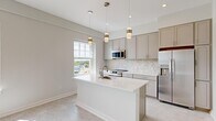 Located at 181 North Main Street in Suffolk, VA, this thoughtfully designed one-bedroom, one-bathroom unit offers a bright and modern living experience on a single floor. The open-concept layout maximizes every inch of the space, creating a seamless flow between the kitchen and living area.

The kitchen is a standout feature, boasting gray shaker-style cabinetry, quartz countertops, and a striking herringbone-patterned tile backsplash. A central island with an undermount sink provides both additional prep space and a natural gathering point. Stainless steel appliances, including a refrigerator, range, and microwave, complete the contemporary look. Pendant lighting adds warmth and visual interest overhead, while large windows invite abundant natural light and outdoor views.

The open living area extends from the kitchen, bathed in natural light from multiple windows that frame views of the surrounding Suffolk cityscape. Light-toned flooring flows consistently throughout the unit, reinforcing the clean, cohesive aesthetic.

The bedroom is a comfortable retreat, featuring a sliding double closet, a bright window with outdoor views, and neutral tones that create a calm atmosphere. The bathroom offers a full tub-shower combination, a white vanity with a taupe countertop, and tile flooring accented with brushed gold hardware. Hallways connect the spaces efficiently, completing this well-appointed and move-in-ready unit.
