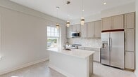 Located at 181 North Main Street in Suffolk, VA, this thoughtfully designed one-bedroom, one-bathroom unit offers a bright and modern living experience on a single floor. The open-concept layout maximizes every inch of the space, creating a seamless flow between the kitchen and living area.

The kitchen is a standout feature, boasting gray shaker-style cabinetry, quartz countertops, and a striking herringbone-patterned tile backsplash. A central island with an undermount sink provides both additional prep space and a natural gathering point. Stainless steel appliances, including a refrigerator, range, and microwave, complete the contemporary look. Pendant lighting adds warmth and visual interest overhead, while large windows invite abundant natural light and outdoor views.

The open living area extends from the kitchen, bathed in natural light from multiple windows that frame views of the surrounding Suffolk cityscape. Light-toned flooring flows consistently throughout the unit, reinforcing the clean, cohesive aesthetic.

The bedroom is a comfortable retreat, featuring a sliding double closet, a bright window with outdoor views, and neutral tones that create a calm atmosphere. The bathroom offers a full tub-shower combination, a white vanity with a taupe countertop, and tile flooring accented with brushed gold hardware. Hallways connect the spaces efficiently, completing this well-appointed and move-in-ready unit.