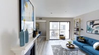 This well-appointed two-bedroom, two-bathroom residence spans a generous single floor, offering an efficient and thoughtfully designed layout. The open-concept living area serves as the heart of the home, featuring light wood-tone flooring that runs throughout and neutral gray walls that create a clean, modern backdrop. A decorative fireplace with a crisp white mantle anchors one side of the living space, providing an elegant focal point.

Large sliding glass doors flood the interior with natural light and open directly onto a private balcony, which offers outdoor seating space — ideal for dining or relaxing. The seamless indoor-outdoor connection enhances the sense of openness throughout the main living area.

The space is further complemented by contemporary details including recessed ceiling vents and smooth white ceilings. A built-in shelving unit along one wall provides functional display and storage options. The overall ambiance is bright, airy, and move-in ready, with a cohesive modern aesthetic defined by clean lines, neutral tones, and purposeful design elements that make the space feel welcoming and versatile.
