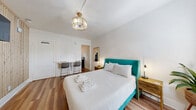 Located at 805 Fourth Ave N in Saint Petersburg, Florida, this efficiently designed one-bedroom, one-bathroom unit offers a thoughtfully curated interior that maximizes every inch of its compact footprint. The main living and sleeping area serves as the heart of the space, centered around a queen bed with a bold teal upholstered frame and complemented by warm wood-look plank flooring that runs throughout. A striking slatted natural wood accent wall anchors the room, providing both texture and visual depth while housing a wall-mounted flat-screen TV. A decorative pendant light fixture adds an elegant focal point overhead, and a wall-mounted mini-split unit ensures climate comfort year-round. A compact workspace with a white-top bar table and modern chairs offers a functional area for work or dining. The kitchen is neatly appointed with white shaker-style cabinetry, matte black hardware, a stainless steel sink, and a stainless steel range, all brightened by a window that draws in natural light. The bathroom features a white vanity with matte black fixtures, a backlit vanity mirror, and light wood-look tile flooring, maintaining the clean, contemporary aesthetic found throughout the unit. A wall-mounted coat rack near the entry provides practical storage in this well-appointed Saint Petersburg residence.