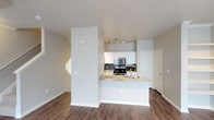 This two-story Dallas property offers a thoughtfully designed open-concept layout on the main level, where the kitchen and living area flow seamlessly together. The kitchen is outfitted with white cabinetry, a dark tile backsplash, and stainless steel appliances, including a gas range with microwave above. A granite-topped peninsula with an integrated sink serves as both a functional workspace and a natural divider between the kitchen and the adjoining living area, making it ideal for casual dining or entertaining. Track lighting above the kitchen ensures ample task illumination. The living area features warm hardwood-style flooring that extends throughout the main level, complementing the neutral wall tones and white trim for a clean, contemporary aesthetic. A staircase is visible along one wall, providing access to the second floor, which expands the overall living space of the home. The layout is practical and efficient, with natural light contributing to a bright and welcoming atmosphere throughout.