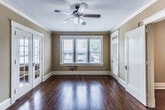 This single-floor residence in Memphis's 38104 zip code blends classic architectural character with functional updates throughout. Rich, warm hardwood floors extend across the living areas and bedroom, complementing crown molding and crisp white trim that reflect the building's traditional style. The spacious living room is a standout, featuring French doors with transom windows, a ceiling fan with light fixture, and large windows fitted with blinds that invite generous natural light while offering views of the surrounding neighborhood.

The layout flows naturally from the living area into the bedroom, which includes closet access and additional doorways that contribute to an open, connected feel. A separate room near the entry features a transom-topped door, a side window, and track lighting overhead. The kitchen is well-appointed with dark espresso cabinetry, light countertops, a gas range, stainless steel microwave, and hardwood flooring continuing throughout.

The bathroom maintains a classic aesthetic with white subway tile surrounding the tub and shower, a black-and-white mosaic tile floor, a vanity with mirror, and a small window providing ventilation and light. Overall, the space offers a cohesive blend of traditional detailing and practical amenities.