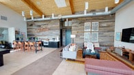 The Ocotillo Clubhouse is a thoughtfully designed single-floor community space that blends rustic warmth with modern amenities. The architecture is defined by dramatic vaulted ceilings clad in warm wood planking, exposed timber beams, and industrial-style ductwork that together create an inviting, lodge-inspired atmosphere. Floor-to-ceiling glass walls and oversized sliding doors flood the interior with abundant natural light while framing sweeping views of the surrounding greenery and outdoor terrace, where additional seating is available.

The main lounge area features a comfortable seating arrangement anchored by a vibrant geometric area rug, a large flat-screen television, and a striking reclaimed wood accent wall adorned with the "Ocotillo" name in bold décor. A billiards table and casual game areas, including a Jenga-topped dining table, provide entertainment options for residents.

The full kitchenette is well-equipped with stainless steel appliances, a side-by-side refrigerator, a coffee station, ample counter space, and a double basin sink — ideal for hosting community gatherings. The open floor plan seamlessly connects all areas, creating a fluid and social environment. Throughout the space, consistent tile flooring, curated artwork, and warm accent lighting contribute to a cohesive, welcoming ambiance suited for both relaxed socializing and organized community events.