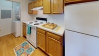 This single-floor residence offers a practical and well-organized layout across several rooms. The living area is generously sized, finished with neutral carpet and equipped with a ceiling fan. A sliding glass door with vertical blinds opens to an outdoor view, filling the space with natural light. The kitchen connects to the living area via a pass-through breakfast bar, and features warm oak cabinetry, light-toned laminate countertops, a coil-burner range with overhead ventilation, and a full-size refrigerator. Hardwood-style flooring runs throughout the kitchen, adding a clean contrast to the carpeted living spaces.

The bedrooms are comfortably sized, each finished with neutral carpet and featuring windows with blinds that allow natural light while maintaining privacy. The rooms offer clean white walls and adequate closet access. Two bathrooms serve the residence; one includes a tub-shower combination with tiled surround, oak vanity, and a well-lit mirror, while the second is a more compact full bath also featuring an oak vanity and hardwood-style flooring. Closet space with built-in shelving is visible near one of the bathrooms, providing useful additional storage throughout the home.