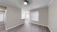 This single-story residence presents a cohesive, modern design highlighted by wood-look plank flooring and warm neutral tones carried consistently throughout. The main living area is generously proportioned, featuring crown molding, a ceiling fan with integrated lighting, and multiple windows fitted with horizontal blinds that allow ample natural light. A built-in arched shelving niche adds a distinctive architectural detail, providing both visual interest and functional display storage.

The kitchen is accessible via a pass-through counter with a clean white surface, ideal for casual dining or serving. Inside, white cabinetry pairs with stainless steel appliances, including a refrigerator and microwave, beneath a skylight that brightens the space further.

The bedrooms are well-sized, each equipped with ceiling fans, windows with outdoor views, and continued wood-look flooring. The primary bedroom connects to a spacious walk-in closet outfitted with multi-level wire shelving and hanging rods along both walls, offering substantial organization capacity. The bathroom features a tiled soaking tub and shower combination with brushed nickel fixtures. Throughout the unit, white baseboards and clean wall finishes contribute to a bright, move-in-ready ambiance.