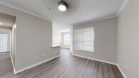 This single-story residence presents a cohesive, modern design highlighted by wood-look plank flooring and warm neutral tones carried consistently throughout. The main living area is generously proportioned, featuring crown molding, a ceiling fan with integrated lighting, and multiple windows fitted with horizontal blinds that allow ample natural light. A built-in arched shelving niche adds a distinctive architectural detail, providing both visual interest and functional display storage.

The kitchen is accessible via a pass-through counter with a clean white surface, ideal for casual dining or serving. Inside, white cabinetry pairs with stainless steel appliances, including a refrigerator and microwave, beneath a skylight that brightens the space further.

The bedrooms are well-sized, each equipped with ceiling fans, windows with outdoor views, and continued wood-look flooring. The primary bedroom connects to a spacious walk-in closet outfitted with multi-level wire shelving and hanging rods along both walls, offering substantial organization capacity. The bathroom features a tiled soaking tub and shower combination with brushed nickel fixtures. Throughout the unit, white baseboards and clean wall finishes contribute to a bright, move-in-ready ambiance.