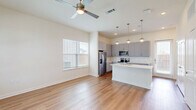 Located in Fort Worth, Texas, this two-story home offers a thoughtfully designed layout across two floors. The main level provides an expansive open-concept living and kitchen area bathed in natural light from multiple windows. The kitchen is a standout feature, showcasing gray shaker-style cabinetry reaching to the ceiling, crisp white quartz countertops, stainless steel appliances including a side-by-side refrigerator and range, and a large central island with pendant lighting overhead — ideal for both cooking and casual dining. Light wood-tone flooring runs throughout the main level, complementing the neutral color palette and creating a warm, cohesive ambiance. The living area is bright and airy, with a ceiling fan and views to the outdoors. Upstairs, the primary bedroom offers a comfortable and private retreat, complete with its own en-suite bathroom featuring a dual-sink vanity with blue cabinetry and quartz countertops, and a spacious walk-in closet with built-in shelving and hanging rods. The second bedroom is generously sized with wood-look flooring and natural light from dual windows. Three full bathrooms serve the home, each finished with modern fixtures. Two well-organized closets with custom built-ins provide ample storage throughout.