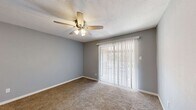 This single-floor residence offers a thoughtfully designed layout with a cohesive, neutral color palette of soft gray walls and white trim throughout. The bedrooms are carpeted in warm beige tones and each features a ceiling fan with integrated lighting, providing both comfort and air circulation. The primary bedroom includes a sliding glass door dressed with vertical blinds, allowing natural light to filter in while offering a view of the outdoors. Each bedroom also includes closet storage, with at least one featuring a six-panel closet door. The kitchen is a functional and attractive space, highlighted by white cabinetry, granite-style countertops, a breakfast bar with elegant geometric pendant lighting, and black appliances including a refrigerator and range. Light wood-look flooring runs through the kitchen and hallway areas, creating a clean contrast to the carpeted rooms. The bathrooms are finished in a classic white palette, each featuring a full tub-shower combination with white subway tile surround and chrome fixtures. Textured ceilings add a subtle design detail consistent throughout the space. Overall, the residence presents a clean, move-in ready environment with practical finishes and a bright, airy ambiance.