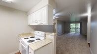 This three-bedroom, one-bathroom residence in Seattle, WA offers a practical and comfortable single-floor layout. The open-concept kitchen and living area serves as the heart of the home. The kitchen features white cabinetry, light laminate countertops, a white electric coil-burner range, a full-size refrigerator, a stainless steel sink, and wood-style flooring — all flowing seamlessly into the carpeted living room. The living room is highlighted by a tile-surround fireplace, a ceiling fan, and a sliding glass door that opens to a balcony with lush greenery views, filling the space with natural light. The three bedrooms are carpeted and serviced by baseboard heating, with windows offering leafy outdoor views. The primary bedroom provides a comfortable amount of space for everyday living. The full bathroom includes a soaking tub with a shower and curtain rod. A hallway connects the main living areas to the bedrooms and closet, supporting an efficient flow throughout the unit. The textured ceilings and neutral gray and beige tones throughout create a clean, cohesive aesthetic. This residence is ideally suited for those seeking a functional layout in the Seattle area.