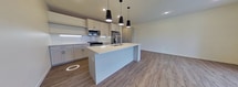 This contemporary 730 square foot apartment offers a thoughtfully designed single-floor living space. The heart of the home is an open-concept area combining the kitchen and living room, creating a seamless flow for modern lifestyles. The kitchen is a standout feature, boasting sleek white cabinetry, stainless steel appliances, and a generous island with a built-in sink, perfect for both meal preparation and casual dining.

Large windows dominate the living areas, flooding the space with natural light and offering expansive views of the surrounding urban landscape. These windows not only brighten the interior but also create a sense of spaciousness and connection to the outdoors.

Throughout the apartment, wood-style flooring adds warmth and continuity, complementing the crisp white walls and modern fixtures. Recessed lighting in the kitchen and living areas provides adjustable illumination options, while stylish pendant lights over the kitchen island add a touch of sophistication.

The layout includes a separate bedroom area and a walk-in closet, offering privacy and ample storage. The overall design emphasizes clean lines and a neutral color palette, creating a versatile canvas for personal styling. This apartment is ideally suited for those seeking a contemporary urban living experience with attention to both form and function.