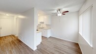 This two-story residence is designed with a clean, neutral aesthetic that creates a bright and functional living environment. The main level features wood-style hard flooring that flows through the living and dining areas, complemented by a ceiling fan with integrated lighting to promote air circulation and comfort. The kitchen is positioned adjacent to the living area and is equipped with white cabinetry, light stone-finish countertops, a gas range, and a stainless steel refrigerator. A pass-through counter connects the kitchen to the main living space, enhancing the open feel of the layout. A hallway leads from the kitchen toward additional rooms and bathroom facilities. One full bathroom on this level includes a tub-shower combination with a curved curtain rod, a vanity with matching countertops, and wood-look tile flooring. A secondary water closet provides an additional convenience. The upper level features carpeted bedrooms with textured ceilings, large windows that allow natural light to fill the space, and views of the surrounding exterior. The staircase connecting both floors is centrally located, making navigation between levels straightforward. Throughout, the space maintains a consistent, understated palette of whites and warm neutrals.