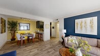 This thoughtfully designed single-floor residence combines bold color choices with functional living spaces to create a warm and inviting atmosphere. The open-concept living and dining area features wood-look flooring that flows seamlessly throughout, anchored by a striking navy blue accent wall in the living room and a cheerful yellow tone in the dining area. The living room offers generous space, large windows dressed with striped curtains that invite natural light, and a wall-mounted television area. A separate sitting room features a vibrant orange accent wall with plush carpeting, adding a cozy and versatile retreat.

The kitchen is well-equipped with dark cabinetry, granite-style countertops, stainless steel appliances including a range, microwave, dishwasher, and refrigerator, all set atop wood-look flooring. Adjacent, the dining area benefits from track lighting and a warm yellow accent, creating an intimate setting for meals.

The bedrooms are carpeted for comfort, each featuring bold accent walls in golden yellow tones, ample natural light from large windows, and generous closet space — including a louvered bi-fold closet in one room. The bathroom is finished with large-format gray stone-look tile surrounding a full soaking tub and shower combination, complemented by wood-look flooring for a cohesive design.