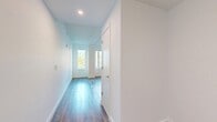 Located at 1300 Fairmount Ave, this efficiently designed 320-square-foot single-floor unit makes excellent use of its space across a kitchen, hallway, and bathroom. The open living area is anchored by rich hardwood flooring and bright white walls, with large windows that invite generous natural light and views of surrounding greenery. The modern kitchen is a standout feature, showcasing bold navy blue lower cabinets contrasted by white upper cabinetry, stainless steel appliances including a full-size refrigerator, electric range with over-range microwave, and dishwasher. A striking geometric mosaic tile backsplash in blue, yellow, and white adds a vibrant, artistic touch, complemented by sleek countertops. The bathroom continues the bold design language with floor-to-ceiling vertical navy blue tile surrounding a full soaking tub and shower, white large-format floor tiles, a wood-toned floating vanity, and clean white upper wall tile. The hallway connects the spaces efficiently, maintaining the unit's clean, contemporary aesthetic throughout. This well-appointed unit combines modern finishes and thoughtful design to maximize comfort and functionality within its compact footprint.