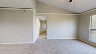 This single-floor, 2-bedroom, 1-bathroom home offers a thoughtfully arranged layout that makes efficient use of its space. The living area immediately impresses with soaring vaulted ceilings, soft wall-to-wall carpeting, and large windows fitted with blinds that allow ample natural light to filter in. A ceiling fan adds both style and comfort to the room. The front entry leads directly into this open area, which connects seamlessly to the rest of the home via a central hallway.

The kitchen features warm, dark wood cabinetry, light stone-finish countertops, stainless steel appliances including an electric range with overhead microwave, and durable wood-look flooring — a clean, functional space well-suited for everyday cooking.

The primary bedroom is a spacious retreat with vaulted ceilings, a ceiling fan, and generous natural light from a large window. The second bedroom is comparably comfortable, offering carpet flooring, a ceiling fan, and a built-in closet with sliding doors. Both rooms maintain the home's neutral, light gray color palette.

The full bathroom includes a tub-shower combination with clean white tile surround, dark wood cabinetry above, and wood-look flooring. A hallway with a closet completes the interior, providing practical storage. Overall, the home presents a clean, neutral aesthetic throughout.