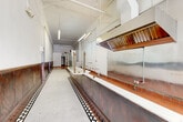 Located at 752 S Main Street in the heart of downtown Los Angeles, this single-floor commercial space blends historic character with functional infrastructure. The storefront entry features a classic glass vestibule door framed by large street-facing windows, offering excellent visibility and natural light from the busy Main Street corridor. Distinctive vintage penny tile flooring with a decorative border pattern anchors the front of the space, transitioning to warm hardwood floors toward the rear — a striking combination that speaks to the building's storied past.

A lengthy service counter runs along one side of the main floor, complete with a stainless steel commercial hood system, plumbing rough-ins, and tiled surfaces, indicating strong existing infrastructure for food and beverage operations. Dark wood wainscoting lines the walls throughout, lending a rich, classic aesthetic to the elongated floor plan. A ceiling fan near the storefront adds to the vintage ambiance, while fluorescent strip lighting illuminates the kitchen corridor.

Toward the rear, terra cotta tile flooring continues through the kitchen area, which includes walk-in cooler panels, additional hood ventilation, and exposed utility connections. A restroom with ADA-accessible fixtures is also present. The space is well-suited for restaurant, café, or retail use, offering a compelling mix of original architectural details and practical commercial amenities.
