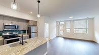This well-appointed 2-bedroom, 2-bathroom single-story residence offers a thoughtfully designed open-concept layout that maximizes functionality throughout its efficiently organized floor plan. The combined kitchen and living area serves as the heart of the home, where rich hardwood-style flooring, recessed lighting, and large windows with exterior door access create a bright, welcoming atmosphere with outdoor views.

The kitchen is equipped with stainless steel appliances, including a refrigerator, range, and microwave, complemented by gray cabinetry, a teal subway tile backsplash, and a generous granite-topped island with an undermount sink and pendant lighting. An in-unit washer is conveniently accessible from the kitchen area.

Both bedrooms feature plush carpeting and ample natural light. The primary bedroom includes access to a spacious walk-in closet with multi-tiered wire shelving. The second bedroom benefits from corner windows that invite additional light. One bathroom features a double-sink granite vanity, pendant lighting, and a tub-shower combination, maintaining the same refined finishes found throughout the residence.