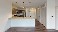 Located in the heart of Rock Hill, SC, this single-floor residence offers a thoughtfully designed layout with contemporary finishes throughout. The open-concept kitchen is a standout feature, showcasing rich dark-toned shaker cabinetry, granite countertops, and a full suite of stainless steel appliances including a range, microwave, and refrigerator. A large kitchen island with pendant lighting above serves as both a functional workspace and a natural gathering point, flowing seamlessly into the adjacent living area. The living space is bright and welcoming, benefiting from a set of French doors that invite natural light and provide access to the outdoors. Durable hardwood-style flooring runs through the main living and kitchen areas, adding warmth and a polished aesthetic. The bedroom is carpeted for comfort, features a ceiling fan, and connects directly to a well-appointed bathroom. The bathroom is finished with granite countertops, dark shaker-style cabinetry, a large vanity mirror, and hardwood-style flooring that continues the cohesive design language of the unit. The overall layout, as seen in the dollhouse view, is efficiently organized with clear distinctions between living, sleeping, and bathroom spaces, making this a clean and functional residence in a convenient downtown location.