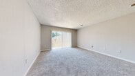 This single-floor, 2-bedroom, 1-bathroom unit offers a practical and comfortable layout across a compact but well-utilized footprint. The living room is a standout space, featuring plush carpeting, neutral walls, a textured ceiling, and a sliding glass door that opens to an outdoor balcony, allowing natural light and views of surrounding greenery to fill the room.

The kitchen is designed for efficiency, featuring a galley-style layout with white cabinetry, light granite-style countertops, a double sink, a dishwasher, and a white electric range. A peninsula with a breakfast bar extends into an adjacent area with rich dark hardwood flooring, creating a natural division between the kitchen and main living spaces.

Both bedrooms are carpeted in the same neutral tones as the living room, each featuring windows with vertical blinds that allow in natural light. The primary bedroom offers a generous footprint and includes a closet, while the second bedroom also benefits from outdoor views through its window. Both rooms feature textured ceilings and clean, neutral walls.

The bathroom is straightforward and functional, equipped with a full tub-shower combo accented by classic white subway tile. Throughout the unit, a consistent palette of soft grays and warm neutrals contributes to a clean, understated ambiance.