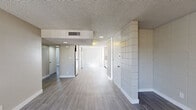 This single-floor residence offers a practical and functional layout across two bedrooms, one bathroom, and a combined kitchen and living area. Throughout the space, light-toned wood-look flooring provides a cohesive aesthetic, complemented by textured ceilings and neutral warm-gray walls that create a clean, understated ambiance.

The open kitchen and living area is anchored by a distinctive white tile-block accent wall that extends from floor to ceiling, adding architectural character to the space. A stainless steel refrigerator is integrated into the kitchen area, and large vertical-blind-covered windows allow abundant natural light to fill the room.

The primary bedroom is a well-proportioned retreat featuring a built-in double closet with sliding doors offering ample storage. The second bedroom is similarly bright, with a window overlooking the outdoors and clean, neutral finishes throughout. Both rooms share the same consistent flooring and textured ceiling treatment.

The bathroom is neatly appointed with a granite-style countertop, an undermount sink with brushed-gold fixtures, a wall-mounted mirror, a soaking tub, and a window that brings in natural light.

A standout functional feature is the in-unit stacked washer and dryer, tucked into a dedicated built-in nook. Central air conditioning with ceiling vents ensures year-round comfort throughout the home.