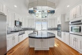 Located in the heart of Beverly Hills on S Elm Drive, this generously sized 5-bedroom, 5-bathroom residence offers a well-appointed single-floor layout designed for comfortable living. The expansive living room is a standout feature, showcasing gleaming hardwood floors, recessed lighting, a classic fireplace, and floor-to-ceiling windows that flood the space with natural light and frame views of lush palm trees outside. The gourmet kitchen is a chef's dream, appointed with white cabinetry, bold blue granite countertops, a large center island, decorative tile backsplash, stainless steel appliances including double wall ovens, and a striking overhead range hood with mirrored accents. The five bedrooms are well-proportioned, with the primary suite offering generous closet space via mirrored sliding doors, plush carpeting, and a dedicated wall-mounted air conditioning unit. Additional bedrooms share a similar clean, bright aesthetic with neutral tones and natural light. The five bathrooms are finished in white tile with glass-enclosed showers and tub combinations. Throughout the residence, the design maintains a crisp, clean palette of white walls and warm flooring, creating a bright and inviting atmosphere befitting its prime Beverly Hills location.