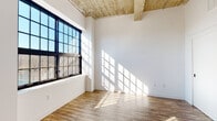 Located at 121 Westmoreland Ave in White Plains, NY, this single-floor loft-style space blends industrial character with modern finishes throughout. The living areas are defined by soaring exposed concrete ceilings with structural beams, warm hardwood flooring, and crisp white walls that create a bright, open atmosphere. Large black-framed industrial-style windows flood the interior with abundant natural light, casting dramatic geometric patterns across the floors and walls.

The contemporary kitchen is well-appointed with two-tone cabinetry — combining high-gloss white upper cabinets with wood-grain lower cabinets — paired with clean white quartz countertops. Stainless steel appliances include a gas range with hood ventilation, a refrigerator, a built-in microwave, and a dishwasher, making this a fully functional and stylish cooking space. Tall pantry-style cabinetry provides ample storage.

The open living and sleeping areas are generously proportioned, benefiting from the soaring ceilings and plentiful window light. Exposed ductwork adds to the loft's industrial aesthetic. The bathroom features neutral large-format tile flooring, two-tone gray and white wall finishes, a wall-mounted sink, and a mirror with overhead lighting, offering a clean and functional design. Overall, the space delivers an urban loft experience with thoughtful modern upgrades.