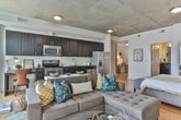 Located in Atlanta's vibrant Old Fourth Ward neighborhood, this modern urban unit at 100 Sixth St NE offers a thoughtfully designed open-concept layout on a single floor. The entryway sets an immediate tone with warm hardwood flooring, an exposed concrete column, and clean white walls that carry throughout the space. The living area is a standout, bathed in natural light from expansive floor-to-ceiling sliding glass doors that open onto a private balcony with open city views of the Atlanta skyline and surrounding urban landscape. An exposed concrete ceiling adds an industrial character that complements the contemporary aesthetic. The kitchen is well-appointed with dark espresso cabinetry, white subway tile backsplash, dark granite countertops, and a full suite of stainless steel appliances, including a side-by-side refrigerator, range, microwave, and dishwasher. The open floor plan seamlessly connects the kitchen, living, and sleeping areas, creating a versatile and airy feel. The bathroom features large-format white tile surrounding a soaking tub and shower combination, accented with a decorative tile border and dark vanity with granite countertop. Hardwood flooring flows consistently throughout the main living spaces, tying the unit together with warmth and continuity.