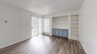 Located at 1930 W Rundberg Ln in Austin, TX, this one-bedroom, one-bathroom unit offers a well-organized single-floor layout with a thoughtful mix of hardwood-style and carpeted flooring throughout. The combined kitchen and living area serves as the heart of the home, featuring wood-style flooring that flows seamlessly between the two spaces. The living room stands out with built-in shelving and cabinetry in a muted blue-gray finish, providing ample display and storage space, along with a sliding glass door that opens to a private balcony and lets in generous natural light. The kitchen is equipped with gray cabinetry, light countertops, and a full suite of black appliances including a refrigerator, electric range, microwave, and dishwasher, complemented by a double-basin sink. The bedroom offers a comfortable and quiet retreat with soft carpeting, a ceiling fan with light fixture, and a window overlooking the outdoors. A dedicated closet provides additional storage. The bathroom features a tub-shower combination, a vanity with matching gray cabinetry and light countertop, hardwood-style flooring, and a mirrored medicine cabinet. Clean white walls and consistent finishes throughout give the space a cohesive, move-in-ready feel.