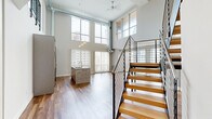 Located in the heart of Detroit at 313 Park Ave, this two-bedroom, two-bathroom residence spans two floors, offering a thoughtfully designed urban living experience. The main floor commands attention with soaring double-height ceilings, floor-to-ceiling windows, and rich hardwood flooring throughout. Abundant natural light pours in, framing sweeping views of the Detroit skyline and cityscape. The open-concept living area features a standout stone-surround linear fireplace, adding a sophisticated focal point to the space. The modern kitchen is equipped with sleek gray cabinetry, granite countertops, a mosaic tile backsplash, stainless steel appliances, and pendant lighting overhead. The upper level, accessible via a contemporary staircase with black metal railings and a wood handrail, hosts additional living space with continued hardwood flooring and generous natural light. Both bedrooms are carpeted and offer large floor-to-ceiling windows with city views. The two bathrooms are finished with clean, modern aesthetics — one featuring a glass-enclosed walk-in shower with large-format tile, and the other with a soaking tub and chevron-patterned tile flooring paired with a granite-topped vanity. Two closets and a hallway complete the well-organized layout.
