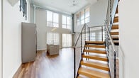 Located in the heart of Detroit at 313 Park Ave, this two-bedroom, two-bathroom residence spans two floors, offering a thoughtfully designed urban living experience. The main floor commands attention with soaring double-height ceilings, floor-to-ceiling windows, and rich hardwood flooring throughout. Abundant natural light pours in, framing sweeping views of the Detroit skyline and cityscape. The open-concept living area features a standout stone-surround linear fireplace, adding a sophisticated focal point to the space. The modern kitchen is equipped with sleek gray cabinetry, granite countertops, a mosaic tile backsplash, stainless steel appliances, and pendant lighting overhead. The upper level, accessible via a contemporary staircase with black metal railings and a wood handrail, hosts additional living space with continued hardwood flooring and generous natural light. Both bedrooms are carpeted and offer large floor-to-ceiling windows with city views. The two bathrooms are finished with clean, modern aesthetics — one featuring a glass-enclosed walk-in shower with large-format tile, and the other with a soaking tub and chevron-patterned tile flooring paired with a granite-topped vanity. Two closets and a hallway complete the well-organized layout.