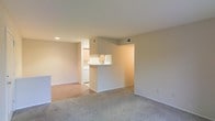 This single-floor space offers a clean, functional layout designed for comfortable everyday living. The living area is finished with plush wall-to-wall carpeting, creating a warm and inviting atmosphere, while recessed lighting provides a well-lit environment throughout. A half-wall pass-through connects the living area to the kitchen, maintaining an open feel while subtly defining each zone. The kitchen features light wood cabinetry, a white appliance suite, and hard-surface flooring that contrasts neatly with the carpeted living space. Neutral-toned walls throughout the unit lend a bright, versatile backdrop that adapts easily to a variety of furnishing styles. Ceiling vents are thoughtfully positioned to ensure consistent climate control across the space. The straightforward, efficient floor plan maximizes usability, making it well-suited for those seeking a low-maintenance, move-in-ready living environment. Overall, the space presents a tidy, understated aesthetic with practical design choices that prioritize comfort and functionality.