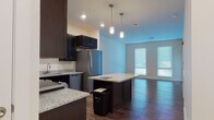 Located at 500 Bank St in New London, Connecticut, this single-floor unit offers a well-designed open-concept layout that seamlessly connects the kitchen and living areas. The kitchen is a standout feature, showcasing rich dark cabinetry, granite countertops, and a full suite of stainless steel appliances including a refrigerator, electric range, dishwasher, and microwave. A central island with pendant lighting above provides additional prep space and a natural gathering point. Durable hardwood-style flooring runs throughout the main living areas, complementing the contemporary aesthetic. Large windows allow natural light to fill the open living space, creating a bright and welcoming atmosphere. The bedroom is finished with plush carpeting and features a window that continues to bring in natural light. The bathroom is distinctly styled with classic black-and-white hexagonal tile flooring, a dark vanity with a white countertop, and a full tub-shower combination with brushed nickel fixtures. Clean white walls and modern hardware throughout the unit contribute to a cohesive, move-in-ready feel. The thoughtful layout and quality finishes make this a well-appointed space in the heart of New London.
