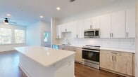 This single-story residence showcases a thoughtfully designed open-concept layout with modern finishes throughout. The kitchen serves as a central highlight, featuring a two-tone cabinet design that pairs crisp white upper cabinets with light natural wood lower cabinets, accented by matte black hardware. A white subway tile backsplash, quartz countertops, stainless steel appliances, and a central island with seating complete the space. Dark hardwood-style flooring runs through the main living and kitchen areas, lending warmth to the bright, white-walled interior.

The living area is generously proportioned, bathed in natural light through a bank of windows fitted with horizontal blinds, and equipped with a ceiling fan. An additional room with direct exterior access via a glass-panel door provides flexible use as a dining area or den.

Bedrooms are carpeted for comfort and receive ample natural light through multiple windows. The primary bathroom features an elongated dual-sink vanity with natural wood cabinetry, quartz countertops, large-format tile flooring, and a separate tiled shower. A secondary bathroom offers a soaking tub with tiled surround. A spacious walk-in closet with wire shelving provides generous storage.