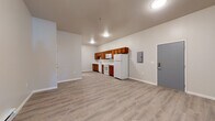 This single-floor unit offers a clean, functional layout designed for comfortable everyday living. The open-concept main area is expansive and airy, anchored by light wood-look luxury vinyl plank flooring that runs throughout the entire space, lending a cohesive and modern feel.

The kitchen is well-appointed with warm-toned medium wood cabinetry, white countertops, and a full suite of white appliances including an electric range, over-the-range microwave, dishwasher, and refrigerator. The galley-style configuration makes efficient use of the space while keeping the kitchen integrated with the main living area.

A structural column provides a subtle architectural division between the kitchen and living zones without interrupting the open flow. The living area is generously sized, offering flexibility for various furniture arrangements. Baseboard heating runs along the perimeter walls, and a wall-mounted mini-split unit provides climate control. Natural light enters through a window in the bedroom area, which also features continuity in the light flooring.

The bathroom is neatly finished with a white vanity, single sink, mirrored medicine cabinet, and brushed nickel hardware accents. Neutral wall tones throughout the unit create a calm, move-in-ready atmosphere that is both practical and inviting.