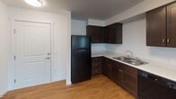 This single-floor unit at 21202 International Blvd in SeaTac, Washington, offers a clean, functional layout designed for comfortable everyday living. The open-concept living area is finished with warm hardwood-style flooring and crisp white walls, creating a bright and welcoming atmosphere. Multiple windows dressed with vertical blinds allow natural light to filter throughout the space, and a glass exterior door provides additional brightness while offering access to an outdoor area.

The kitchen is well-appointed with dark espresso-toned cabinetry, light countertops, and a full suite of black appliances including a range, over-the-range microwave, dishwasher, and refrigerator. The L-shaped layout provides ample counter and storage space, making the kitchen both practical and visually grounded.

The bedroom is carpeted for comfort and features a window with natural light, along with generous closet storage accessible through paneled white doors. The bathroom is finished with matching dark cabinetry, a wide vanity with a large mirror, light countertops, a full bathtub, and hardwood-style flooring, maintaining a consistent design aesthetic throughout the unit.