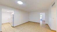 Located in Miami, FL, this single-story, one-bedroom, one-bathroom unit offers a practical and well-organized layout finished consistently with light beige ceramic tile flooring throughout. The combined living and dining area forms the heart of the unit, providing an open, airy feel with clean white walls and ceiling-mounted lighting. Natural light filters in from a balcony access point at the far end, bringing a sense of openness to the space. Adjacent to the living area, the kitchen is efficiently designed with white cabinetry, speckled quartz-style countertops, and white appliances including a refrigerator, electric range, and over-the-range microwave. A pantry provides additional storage. A dedicated den offers flexible use as a home office or secondary lounge area, and a hallway connects the main living spaces to the private quarters. The bedroom is a comfortable size, featuring a window that brings in natural light and views of surrounding greenery. Three closets throughout the unit ensure ample storage. The bathroom is outfitted with floor-to-ceiling beige tile surrounding a full soaking tub with shower, complemented by matching tile flooring and a vanity with a light stone-finish countertop.