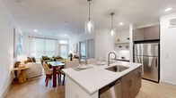 This thoughtfully designed 2-bedroom, 2-bathroom residence offers a cohesive modern aesthetic across its single-floor layout. The open-concept kitchen and living area serves as the heart of the home, anchored by a generous island with white quartz countertops and seating for multiple guests. Sleek two-tone cabinetry in warm wood tones pairs with stainless steel appliances, including a full-size refrigerator and range, while pendant lighting adds a refined touch overhead. Light hardwood flooring flows seamlessly throughout the entire space, enhancing the bright, airy ambiance.

The living room receives abundant natural light through large windows, creating a welcoming atmosphere. The primary bedroom is a spacious retreat featuring a ceiling fan, direct access to an en-suite bathroom with a dual-sink vanity, wood cabinetry, and a glass-enclosed shower. A dedicated walk-in closet with wire shelving provides generous storage. The second bedroom is well-proportioned with ample natural light and closet access. The second bathroom features a stylish vanity with white countertops, a framed mirror, and overhead lighting. Clean white walls and consistent finishes throughout lend the entire residence a polished, contemporary feel.