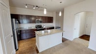 Located in Grand Prairie, TX, this single-floor residence offers a thoughtfully designed layout that balances functionality and comfort. The kitchen serves as a central highlight, showcasing rich dark-wood cabinetry, granite countertops, and a full suite of stainless steel appliances including a refrigerator, electric range, and built-in microwave. A central island with an integrated sink and pendant lighting overhead adds both style and practicality, while track lighting illuminates the workspace throughout. Wood-style flooring anchors the kitchen, transitioning seamlessly into the adjoining living areas.

The living and dining spaces are carpeted and bathed in natural light, with French doors leading to an outdoor area framed by lush greenery — ideal for enjoying the Texas scenery. Ceiling fans provide comfort throughout the main living areas.

The primary bedroom is generously sized with dual windows, plush carpet, and direct access to a spacious walk-in closet with built-in shelving. The en-suite primary bathroom features a dual-sink vanity with dark cabinetry, a separate glass-enclosed shower, and wood-look tile flooring. A secondary bathroom offers a full tub-shower combination with white tile surround. The overall palette of neutral tones and clean finishes creates a bright, welcoming atmosphere throughout.