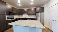 This single-floor residence showcases a cohesive contemporary design throughout. The kitchen serves as a centerpiece, featuring dark espresso-toned cabinetry with sleek bar-pull hardware, granite countertops, and a full suite of stainless steel appliances including a range, microwave, dishwasher, and refrigerator. A white subway tile backsplash adds a clean contrast to the dark cabinetry, while a substantial kitchen island with matching granite provides additional prep and gathering space. Wood-look plank flooring runs throughout the main living areas, contributing to a warm, unified aesthetic.

The open living area adjoins the kitchen seamlessly and is bathed in natural light from a set of French doors that lead to an outdoor space. A ceiling fan serves both the living area and, separately, the bedroom. The bedroom features plush carpeting, a ceiling fan with integrated lighting, and a window that brings in additional natural light.

The bathroom is finished with wood-look flooring consistent with the rest of the unit and includes a full-size soaking tub with shower combination, clean white surround, and dark cabinetry for storage. The overall palette of the unit is neutral and contemporary, creating a bright and functional living environment.