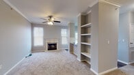 This 2-bedroom, 2-bathroom unit at The Pont Du Guard in Little Rock, Arkansas, offers a well-designed single-floor layout with a cohesive neutral color palette and consistent finishes throughout. The living room serves as the heart of the unit, highlighted by a classic white-mantled fireplace flanked by windows that allow natural light to fill the carpeted space. Crown molding and a ceiling fan add refined detail, while built-in open shelving and a built-in desk area provide functional storage and workspace directly adjacent to the living area. The kitchen features granite countertops, white shaker-style cabinetry, a subway tile backsplash, a stainless steel double-basin sink, and wood-look flooring. An in-unit laundry area is conveniently accessible from the kitchen. Both bedrooms are carpeted and feature ceiling fans and crown molding, with the primary bedroom offering direct access to an en-suite bathroom. Each bathroom is finished with granite-top white vanities, wood-look flooring, and a tiled shower-tub combination. The second bathroom mirrors this design, maintaining a consistent aesthetic across the unit. Windows in each bedroom provide natural light and exterior views.