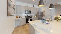 This thoughtfully designed one-bedroom, one-bathroom apartment at 100 Woodside Court in Trumbull, Connecticut offers a modern, open-concept layout with clean lines and contemporary finishes throughout. Light-toned hardwood flooring flows seamlessly across the entire living space, creating a cohesive and airy atmosphere.

The kitchen is a standout feature, outfitted with gray shaker-style cabinetry, white quartz countertops, a classic subway tile backsplash, and a full suite of stainless steel appliances including a gas range, microwave, and refrigerator. A central kitchen island with bar seating and stylish pendant lighting provides both additional prep space and a casual dining area.

The open living area benefits from natural light through a large window and offers a comfortable, inviting atmosphere with neutral-toned walls. The bedroom is well-proportioned, featuring a window with outdoor views and generous built-in closet storage with shelving.

The bathroom is cleanly appointed with a white vanity, quartz countertop, and modern fixtures. Throughout the unit, recessed lighting and crisp white walls contribute to a bright, contemporary feel that makes this single-floor residence a refined and functional living space.