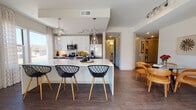 Located at 1115 Town Creek Dr in Austin, Texas, this single-floor residence offers a thoughtfully designed open-concept layout with modern finishes throughout. The kitchen serves as the centerpiece of the living area, featuring crisp white upper cabinetry, dark lower cabinets, a large waterfall-edge island with bar seating, and striking glass pendant lighting. Stainless steel appliances, including a French door refrigerator, built-in microwave, and range, complete the chef-inspired space. Dark hardwood-style flooring runs throughout the main living areas, creating a warm contrast to the bright white surfaces. The living area is bathed in natural light, courtesy of large sliding glass doors that open onto a private balcony with views of the surrounding neighborhood. The bedroom is a calm, neutral retreat with continued hardwood-style flooring and a tray ceiling detail. The en-suite bathroom is finished with large-format marble-look tile flooring, a dual-sink vanity with quartz countertops, framed mirrors, a deep soaking tub, and a separate glass-enclosed walk-in shower. Track lighting and recessed fixtures provide ample illumination throughout. The overall ambiance is clean, contemporary, and well-appointed, reflecting the modern urban lifestyle of Austin.