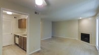 This single-floor residence offers a straightforward and functional layout designed for comfortable everyday living. The open living area is bright and welcoming, finished with light-toned carpet and a ceiling fan with integrated lighting that provides both airflow and illumination. Neutral beige walls and white trim run throughout, lending the space a clean and cohesive aesthetic.

Adjacent to the living area, the kitchen is efficiently arranged and features warm wood-toned cabinetry, a double-basin sink, and tile flooring that defines the space from the carpeted living zone. The cabinetry provides ample storage, and the layout supports practical meal preparation.

Transition spaces include a hallway visible from the main living area, suggesting additional rooms beyond, such as bedrooms or a bathroom. HVAC ventilation is visible in the ceiling, indicating a central air system throughout the unit. The overall design is modest and utilitarian, with clean lines and a neutral palette that offers a blank canvas for personalization. The space is well-suited for those seeking a low-maintenance, move-in-ready residence with a functional open-plan feel.