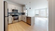 Located at 5000 Libbie Mill East Blvd in Richmond, Virginia, this modern single-floor residence offers a clean, contemporary design with a bright and airy atmosphere throughout. Light-toned hardwood-style flooring flows seamlessly across the open-concept living and dining areas, complemented by crisp white walls that amplify the natural light streaming in through multiple large windows with slatted blinds.

The well-appointed kitchen is a functional centerpiece, featuring white shaker-style cabinetry with matte black hardware, a blue-gray subway tile backsplash, light quartz countertops, and a full suite of stainless steel appliances including a refrigerator, range, microwave, and dishwasher. Pendant lighting hangs above the peninsula, which provides additional prep space and casual seating. The entry area is conveniently positioned adjacent to the kitchen.

The bedrooms are generously proportioned, each bathed in natural light and equipped with closet space, including a walk-in closet in one room. The bathrooms are finished with neutral tile flooring, quartz vanity tops, and white cabinetry. One bathroom includes a shower-tub combination, while another features a dedicated walk-in shower with built-in shelving. The overall design reflects a modern, move-in-ready aesthetic.