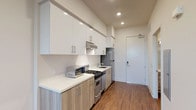 This thoughtfully designed single-floor unit combines contemporary finishes with a clean, functional layout. The galley-style kitchen is a standout feature, outfitted with two-tone cabinetry — crisp white upper cabinets paired with light wood-grain lower cabinets — all complemented by white quartz countertops. Stainless steel appliances, including a gas range, dishwasher, and refrigerator, complete the well-appointed kitchen, while recessed lighting overhead keeps the space bright and inviting. Rich hardwood flooring flows consistently throughout the entire unit, lending warmth and cohesion to every room. The open living area is generously proportioned, featuring a built-in sliding-door closet and direct sightlines to both the kitchen and entry. A dedicated bedroom benefits from a large window that frames outdoor greenery and fills the room with natural light, creating a calm and airy atmosphere. The bathroom is finished with elegant white subway tile in a frameless glass-enclosed walk-in shower, accented with neutral tile trim details and chrome fixtures, adding a polished, spa-like quality. Recessed lighting and clean white walls throughout the unit reinforce a modern, minimalist aesthetic that is both practical and refined.