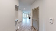 This single-floor space showcases a cohesive modern design defined by light wood-look flooring, crisp white walls, and matte black hardware accents throughout. The entry hallway features a louvered interior door and recessed built-in shelving, offering both functional storage and architectural character as it opens toward the main living area.

The kitchen is well-appointed with flat-front cabinetry in a warm wood tone, quartz countertops, stainless steel appliances, a stylish herringbone tile backsplash, and a built-in wine rack. Matte black pendant lights and fixtures add a contemporary contrast. The kitchen flows seamlessly into the open living and dining area, which benefits from abundant natural light through multiple windows fitted with white blinds. A glass-paned exterior door provides access to an outdoor area, further enhancing the bright, airy atmosphere. A ceiling fan with integrated lighting serves the living space.

The bedrooms are generously proportioned, each featuring natural light from sizable windows with outdoor views of greenery. The bathrooms are finished to a high standard, including a dual-sink vanity with quartz countertops, dark wood cabinetry, framed mirrors, and well-lit surroundings, complemented by a tiled walk-in shower visible in the primary bath.