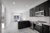 Located at 102 W Main St in Smithtown, NY, this thoughtfully designed one-bedroom, one-bathroom residence offers a clean, modern aesthetic throughout its single floor. Marble-look porcelain tile flooring flows seamlessly across every room, creating a bright, cohesive atmosphere enhanced by crisp white walls and recessed lighting.

The open-concept kitchen is a standout feature, showcasing dark charcoal shaker-style cabinetry with matte black hardware, white quartz countertops, and a classic subway tile backsplash. A peninsula with a brass-finished faucet and undermount sink anchors the space, while a full suite of stainless steel appliances — including a refrigerator, electric range, dishwasher, and over-the-range microwave — ensures full functionality.

The bedroom is a sun-filled retreat, benefiting from large windows that invite abundant natural light and offer views of the surrounding Smithtown streetscape. A wall-mounted PTAC unit provides climate control.

The bathroom is elegantly appointed with a full glass-enclosed walk-in shower clad in white subway tile, finished with matte black fixtures including a rainfall showerhead and a handheld sprayer — delivering a spa-like experience. The overall design of this residence balances modern style with practical comfort in a compact, efficient layout.