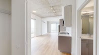 Located in Chicago's vibrant Lincoln Park/Old Town area, this single-floor unit at 1450 N Dayton Street showcases a contemporary industrial-modern design. The open-concept living area is defined by exposed concrete ceilings fitted with track lighting, light wood flooring throughout, and floor-to-ceiling windows that flood the space with natural light while offering expansive views of the Chicago skyline and surrounding cityscape. A wall-mounted split HVAC unit ensures year-round comfort.

The kitchen is thoughtfully designed with two-tone cabinetry—combining white upper cabinets and gray lower units—complemented by a classic white subway tile backsplash, sleek countertops, and a full suite of stainless steel appliances including a refrigerator, dishwasher, range, and built-in microwave. A kitchen island with an undermount sink adds functional workspace.

Two bathrooms serve the unit, each featuring light wood-style flooring, gray cabinetry with gold hardware, and clean white fixtures. One bathroom includes a tiled shower surround. The overall aesthetic is clean, minimalist, and modern, with industrial accents lending character and depth throughout the space.