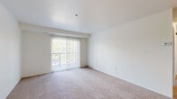 This single-floor residential unit offers a clean, functional layout across several well-defined areas. The living room serves as the central gathering space, featuring wall-to-wall carpeting and a large sliding glass door dressed with vertical blinds that opens to an outdoor balcony or patio, allowing natural light and views of surrounding greenery to flow into the room. The clean white walls and neutral tones create a bright, open ambiance throughout.

The kitchen is efficiently designed with ample cabinetry — including both upper and lower storage — laminate wood-style flooring, a white electric range, refrigerator, and a functional range hood. The kitchen connects openly to the carpeted living area, supporting an easy flow between the two spaces.

The bedroom is comfortably sized with plush carpeting, crisp white walls, and a dedicated closet for storage. A secondary carpeted room with its own entry door provides additional flexible living space.

The bathroom features wood-style vinyl flooring, a wide vanity with an integrated sink and countertop, a large mirror, and a window that introduces natural light. A dedicated utility room houses the water heater, electrical panel, and laundry hookups, offering practical in-unit convenience. Throughout, the unit maintains a consistent, neutral aesthetic that is move-in ready.