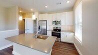 Located at 1980 Icon Way in Knoxville, TN, this well-appointed residence combines modern design with functional living. Rich, dark hardwood-style flooring flows consistently throughout the space, providing a warm and cohesive aesthetic from room to room.

The kitchen serves as a central highlight, featuring crisp white shaker cabinetry, a classic subway tile backsplash, stainless steel appliances including a French door refrigerator, electric range, and over-the-range microwave. A generously sized island with a quartz-style countertop and undermount sink offers both prep space and casual seating, while pendant lighting adds a refined touch overhead.

The living and bedroom areas are bright and airy, benefiting from large windows that invite natural light and offer views of the surrounding greenery. Ceiling fans are present throughout, enhancing comfort in each room. The open layout transitions smoothly between spaces, with a half-wall staircase landing adding architectural interest.

The bathroom is finished with deep charcoal subway tile surrounding a soaking tub and shower combination, complemented by a clean white vanity and wood-look flooring that ties back to the rest of the home. Louvered closet doors and clean white trim complete the polished interior. A staircase with patterned carpet runner connects to additional areas of the home.